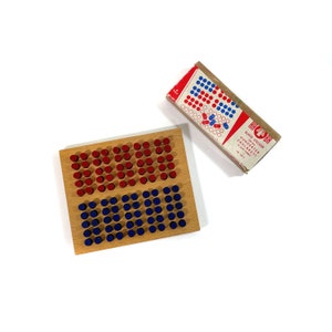 May include: A wooden board with red and blue pegs arranged in a grid pattern. The board is labelled "Blaue Sticker zum Spiel "Hunderter Zahlenbrett".