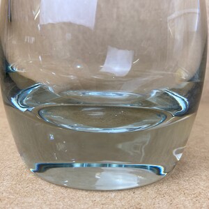 Puede incluir: Un jarr&oacute;n de vidrio transparente con fondo redondeado y boca ancha. El jarr&oacute;n tiene un ligero tono azul.