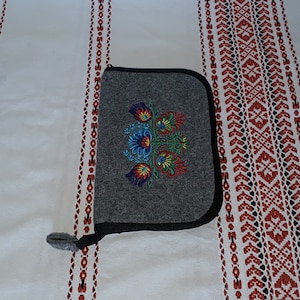 May include: A gray felt pouch with a black zipper and a colorful embroidered floral design.