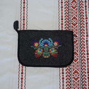 May include: A small gray felt pouch with a colorful embroidered floral design. The pouch has a zipper closure and a small loop at the top.