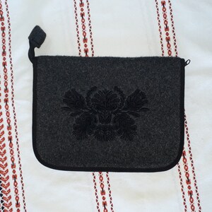 May include: A gray felt pouch with a black embroidered floral design. The pouch has a zipper closure and a black handle.
