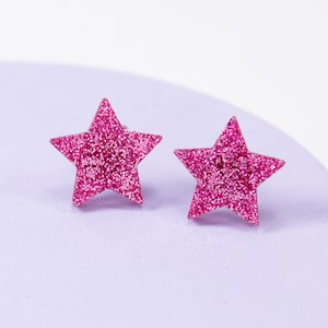 Può includere: Un paio di orecchini a forma di stella con glitter rosa.
