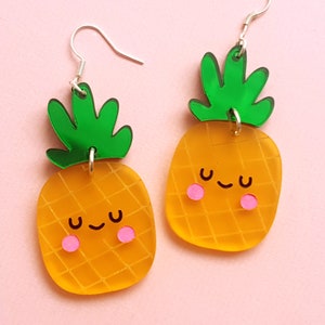 Könnte beinhalten: Ein Paar gelbe Ananas-Ohrringe mit grünen Blättern und rosa Wangen. Die Ohrringe haben silberne Haken.