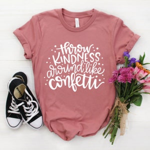 May include: A dusty rose t-shirt with the text "Throw Kindness Around Like Confetti" in white lettering.