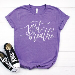 May include: Purple t-shirt with the text "just breathe" in white cursive lettering.
