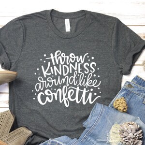 May include: A dark gray t-shirt with white text that reads "Throw Kindness Around Like Confetti".