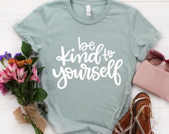 May include: A light blue t-shirt with the text "be kind to yourself" in white script lettering.