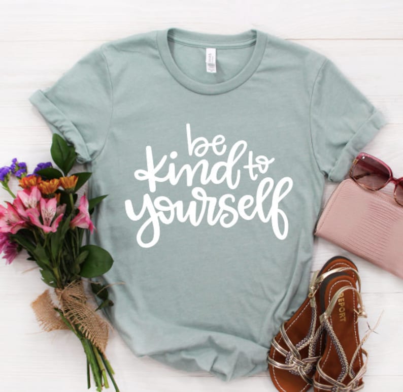May include: A light blue t-shirt with the text "be kind to yourself" in white script lettering.