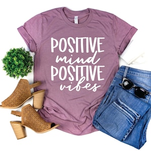 May include: A mauve t-shirt with the text "POSITIVE mind POSITIVE vibes" in white lettering.