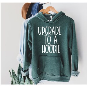 Pu&ograve; includere: Una felpa con cappuccio verde scuro con una grafica bianca che dice "Upgrade to a Hoodie".