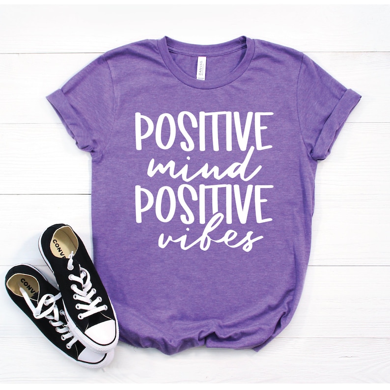 May include: Purple t-shirt with the text "POSITIVE mind POSITIVE vibes" in white lettering.