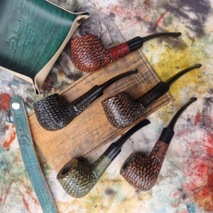Peut inclure: Quatre pipes différentes avec différents motifs de grain de bois et finitions. Les pipes sont en bois brun foncé, noir et vert. Les pipes sont disposées sur une surface en bois avec un plateau en cuir vert en arrière-plan.