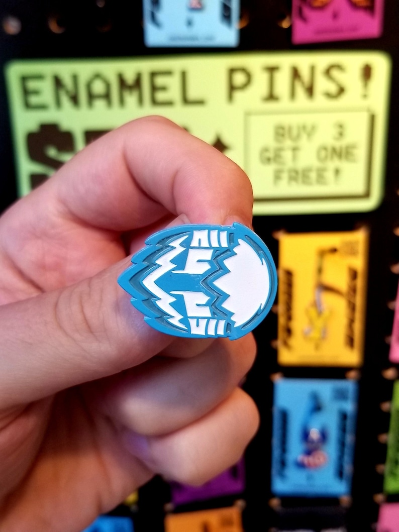 Op de afbeelding: Een blauwe emaille pin met een wit bliksemontwerp. De pin is gevormd als een bliksem en heeft het woord "FREE" erop.