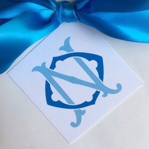 May include: A white card with a blue and light blue monogram of the letters "N" and "C" in a shield shape.