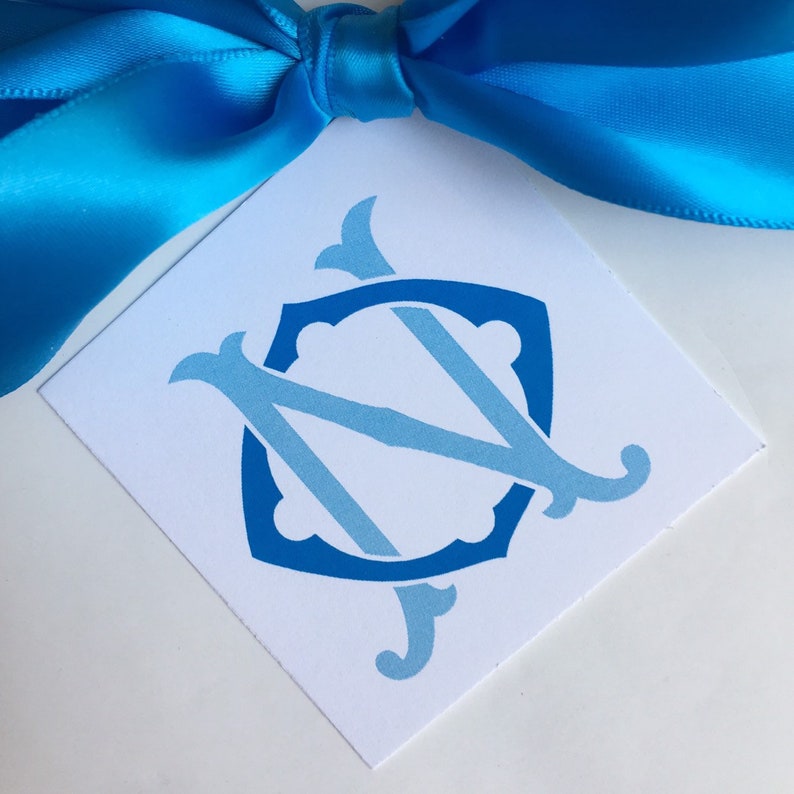 May include: A white card with a blue and light blue monogram of the letters "N" and "C" in a shield shape.