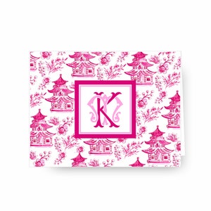 May include: Pink and white stationery card with a repeating pattern of pink pagodas and floral designs. The card features a large pink monogram "K" in the centre.