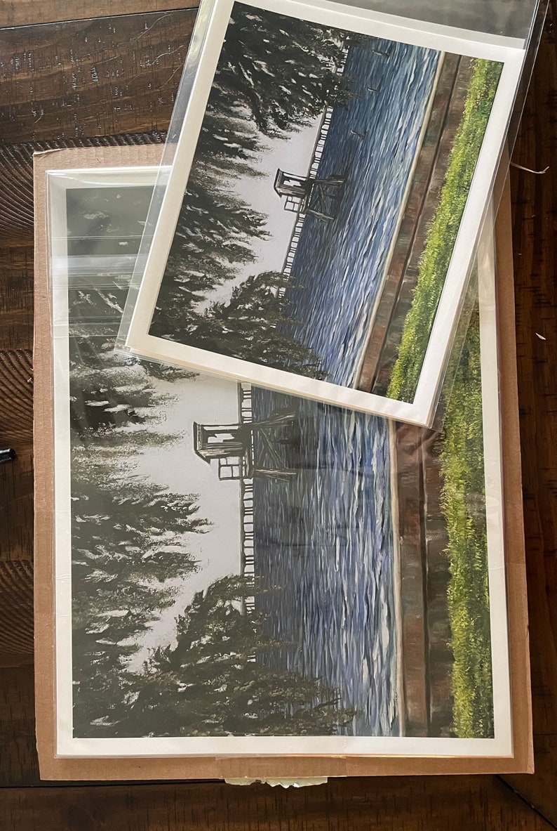 Pu&ograve; includere: Un dipinto ad acquerello incorniciato che rappresenta una scena di lago con una piccola struttura in legno sul bordo dell'acqua. L'acqua &egrave; di un blu profondo con increspature bianche. La struttura &egrave; circondata da alberi e erba verdi.