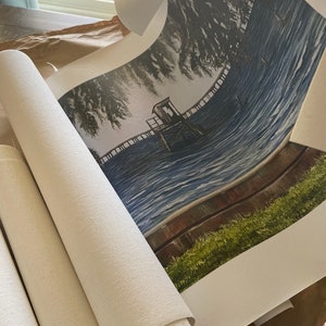 Pu&ograve; includere: Una stampa su tela arrotolata di un dipinto che raffigura un molo di legno che si estende su un lago blu con una piccola struttura in legno sul molo. Il dipinto &egrave; incorniciato da un'area verde erbosa e una recinzione in legno marrone.