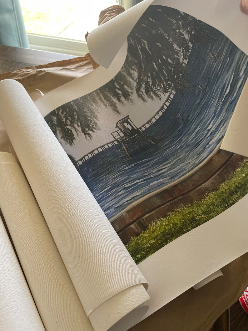 Pu&ograve; includere: Una stampa su tela arrotolata di un dipinto che raffigura un molo di legno che si estende su un lago blu con una piccola struttura in legno sul molo. Il dipinto &egrave; incorniciato da un'area verde erbosa e una recinzione in legno marrone.