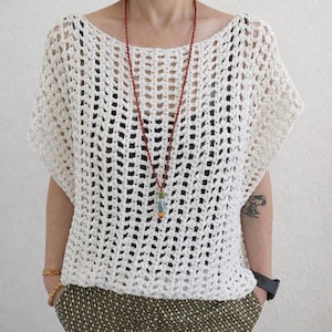 May include: A cream-colored, short-sleeved crochet top with an open, grid-like pattern. The garment is worn over a black base layer and is paired with a long, thin red beaded necklace featuring a multi-colored pendant at the bottom.