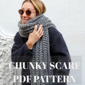 Könnte beinhalten: Ein grauer, grob gestrickter Schal ist um den Hals und die Schultern einer Person gewickelt. Der Schal ist dick und scheint handgefertigt zu sein. Der Text "CHUNKY SCARF PDF PATTERN" wird unten im Bild angezeigt.