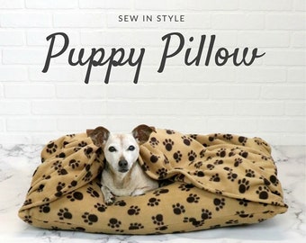 May include: A brown and tan dog bed with a paw print pattern. The bed has an attached blanket that is tucked in around a small dog. The text "Sew in Style" and "Puppy Pillow" is at the top of the image. The text "Sallie Tomato" is at the bottom of the image.