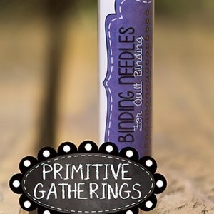 May include: A clear plastic tube with a white lid and a purple label that reads "Binding Needles for Quilt Binding". The tube is sitting on a wooden surface with a black and white sign that reads "Primitive Gatherings".