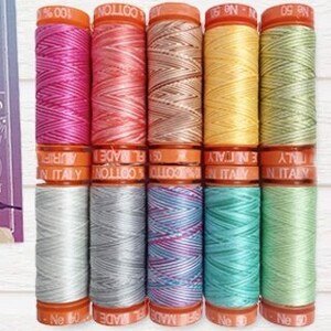 May include: A set of 10 spools of Aurifil 100% cotton thread in various colors, including pink, peach, yellow, and green. The spools are labeled "Aurifil" and "Made in Italy".
