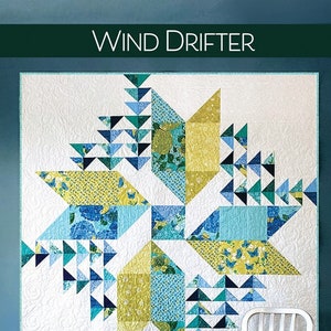May include: A quilt pattern called "Wind Drifter" by Robin Pickens Quilt Patterns. The quilt is made with a fat eighth-friendly pattern in two sizes. The quilt is a mix of blue, green, and yellow fabrics. The quilt is hanging on a wall with a white chair in front of it.