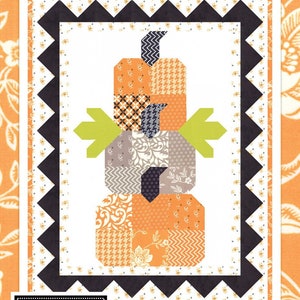 May include: A quilt pattern titled Pumpkin Trio featuring a central stacked pumpkin design made of orange, gray, and black patterned fabric blocks with green leaf accents. The border consists of black triangles on a white floral background.