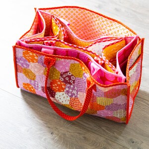 May include: A pink and orange patchwork tote bag with multiple pockets and a red handle.