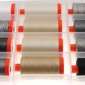 May include: A clear plastic storage container holding twelve spools of sewing thread in various shades of white, gray, black, and beige. Each spool features bright orange end caps and is organized into individual compartments within the tray.