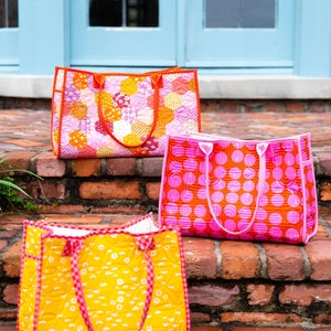 May include: Three quilted tote bags in different patterns. The top bag is pink and white with a geometric pattern. The middle bag is pink with large white polka dots. The bottom bag is yellow with a small white floral pattern.