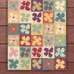 May include: A quilt pattern called "Crazy Blooms" with a patchwork design of colorful floral shapes. The pattern is designed by One Sister Designs.