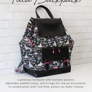 May include: Black Tula backpack with a flap closure and multiple pockets. The backpack features a pattern of seals and colorful clouds. It has adjustable padded straps and d-rings. The text "Tula Backpack" is displayed at the top.