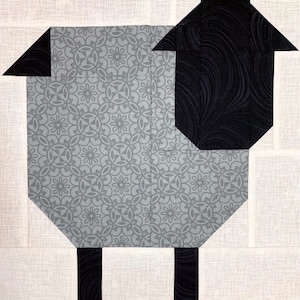 May include: A gray and black patchwork quilt block depicting a sheep. The sheep has a black head and legs and a gray body with a floral pattern.