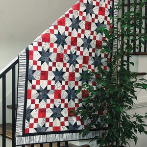 May include: A red, white and black patchwork quilt with a star pattern. The quilt is hanging on a staircase railing.