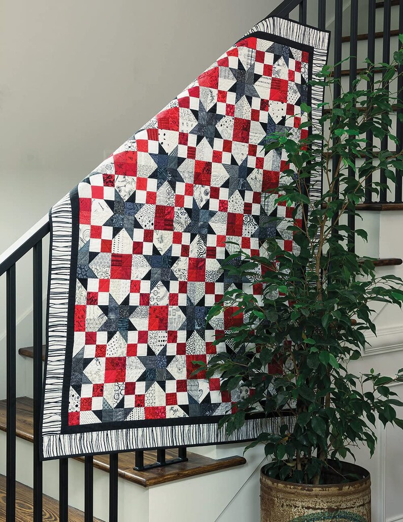 May include: A red, white and black patchwork quilt with a star pattern. The quilt is hanging on a staircase railing.