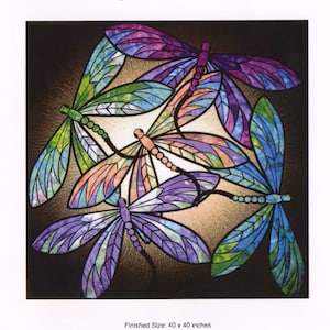 May include: A stained glass design featuring five dragonflies in shades of purple, blue, green, and orange. The artwork is titled "Dance of the Dragonflies" and is designed by JoAnn Hoffman. Finished size is 40 x 40 inches.