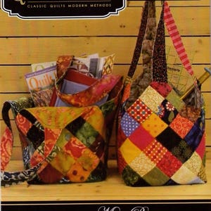 May include: Two patchwork fabric tote bags with colorful squares. The bags have different strap designs and are filled with magazines and other items. The image includes the text "Quiltsmart" and "Midi Bag".