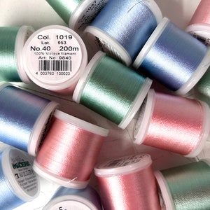 May include: A collection of embroidery thread spools in pastel shades of pink, blue, and green. Each spool features a white label with black text, including Col. 1019, Lot 953, No. 40, 200m, 100% Viscose filament, and Art. No. 9840, along with a barcode.