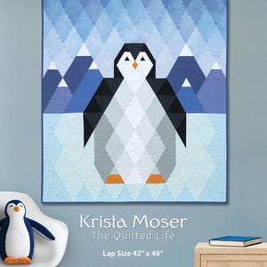 May include: A geometric quilt featuring a penguin design with a blue and white color scheme. The quilt measures 42 inches by 48 inches. The text "PERCY the PENGUIN" is at the top. A stuffed penguin sits on a white chair.