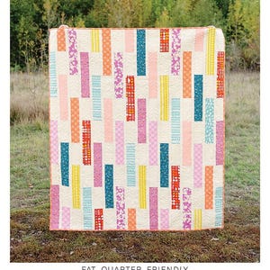 May include: The Talia Quilt pattern by Erica Jackman. A colorful quilt with vertical rectangular blocks in various patterns and colors, including pink, orange, blue, and yellow, on a cream background. The quilt is displayed outdoors.