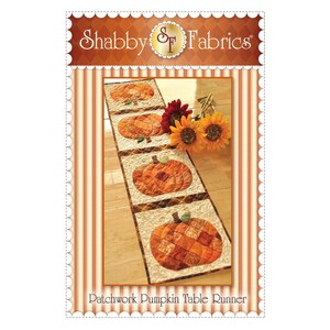 K&ouml;nnte beinhalten: Ein Patchwork-Tischl&auml;ufer mit f&uuml;nf orangefarbenen K&uuml;rbissen in einer Reihe. Der L&auml;ufer liegt auf einem Holzboden mit einem Sonnenblumenstrau&szlig; im Hintergrund. Der Text "Patchwork Pumpkin Table Runner" befindet sich am unteren Rand des Bildes.