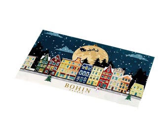 Könnte beinhalten: Eine rechteckige Karte mit einer winterlichen Nachtszene, bunten Häusern, einem großen gelben Mond und der Silhouette eines Weihnachtsschlittens. Der Text BOHIN FRANCE ist in Gold auf einer verschneiten Landschaft mit Bäumen gedruckt.