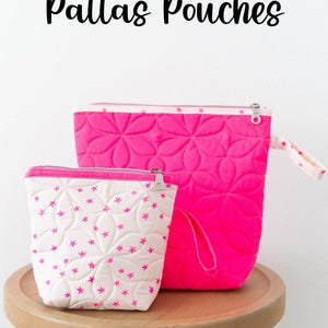 May include: Two pink quilted pouches with zipper closures. The smaller pouch has a white background with pink stars. The larger pouch has a pink background with a quilted flower pattern. The pouches are sitting on a wooden stool. The text "Pallas Pouches" is at the top of the image. The text "Knot + Thread design" is at the bottom of the image.