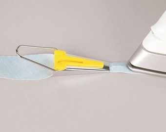 May include: A yellow and silver seam guide tool for sewing, being used to press a seam on a light blue fabric with an iron.