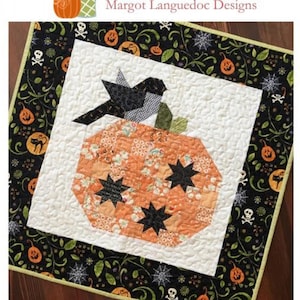 May include: A square quilted wall hanging featuring a central orange pumpkin block with black star accents and a black bird perched on top. The pumpkin is set against a white background with a black border printed with pumpkins, skulls, and spiderwebs.