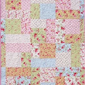 May include: A patchwork quilt with a floral pattern in shades of pink, green, blue, and yellow. The quilt is made up of squares of different sizes and is quilted with a swirl pattern.