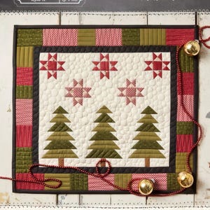 May include: A quilt pattern featuring a winter scene with three green pine trees and red stars on a white background. The quilt is surrounded by a red, green, and black border. The quilt is titled "Winter Pines Quilt" and measures 18.5 inches by 20.5 inches.